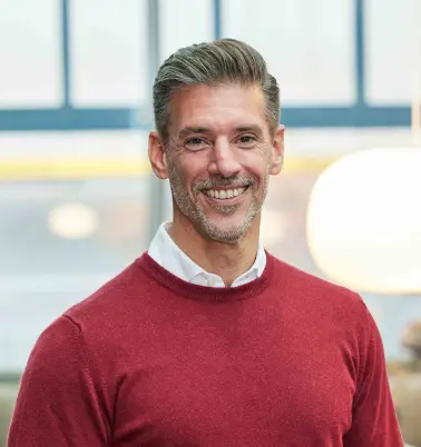 Andreas Tiedtke steht in einem Büro, schaut nach vorne und lächelt. 
