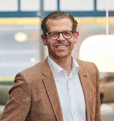 Tobias von Mäßenhausen steht in einem Büro, schaut nach vorne und lächelt. 