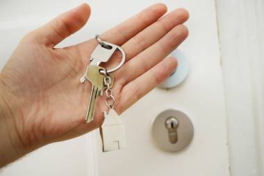 Eine Hand hält einen Schlüssel vor einer Haustür.