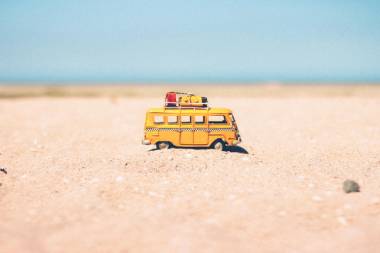 Gelbes Wohnmobil mit Gepäckstücken auf dem Dach steht im Sand.