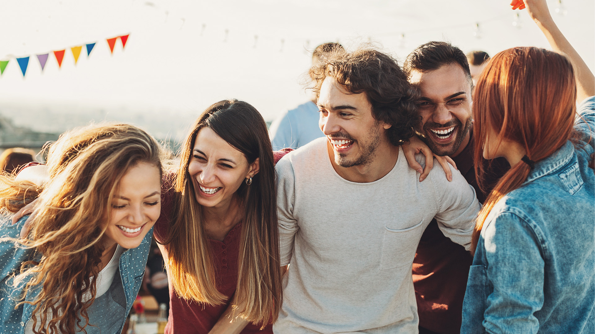 Fünf Personen liegen sich in den Armen und feiern eine Party. Alle lachen ausgelassen. 