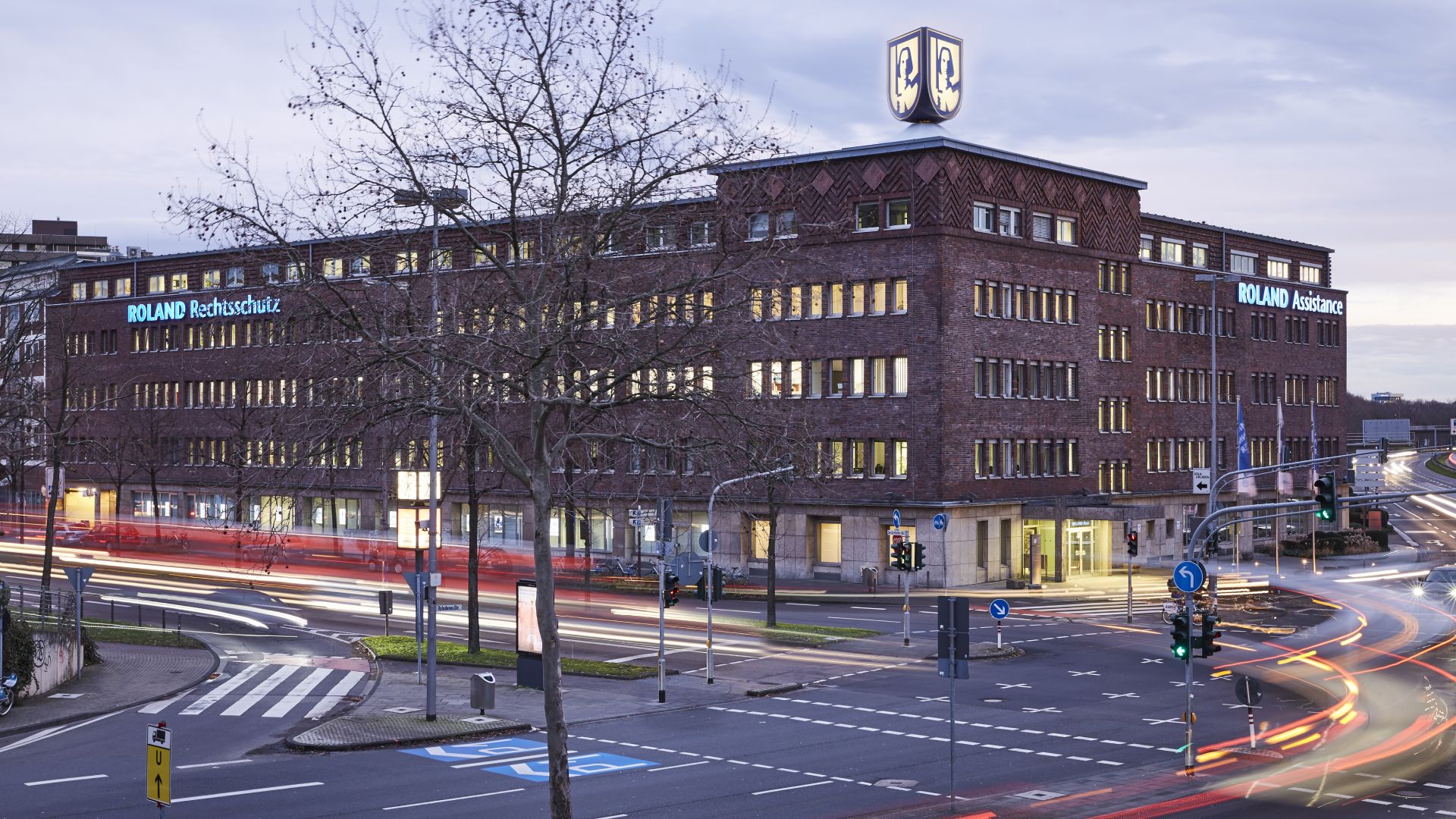Großes Bürogebäude mit 4 Etagen steht an Hauptstraße. Auf dem Gebäude ist das ROLAND Logo. An dem Gebäude steht