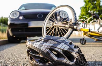 Auf einer Straße liegen ein Fahrrad und ein Fahrradhelm. Im Hintergrund ist ein Auto zu sehen.