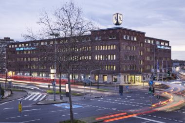 Großes Bürogebäude mit 4 Etagen steht an Hauptstraße. Auf dem Gebäude ist das ROLAND Logo. An dem Gebäude steht 